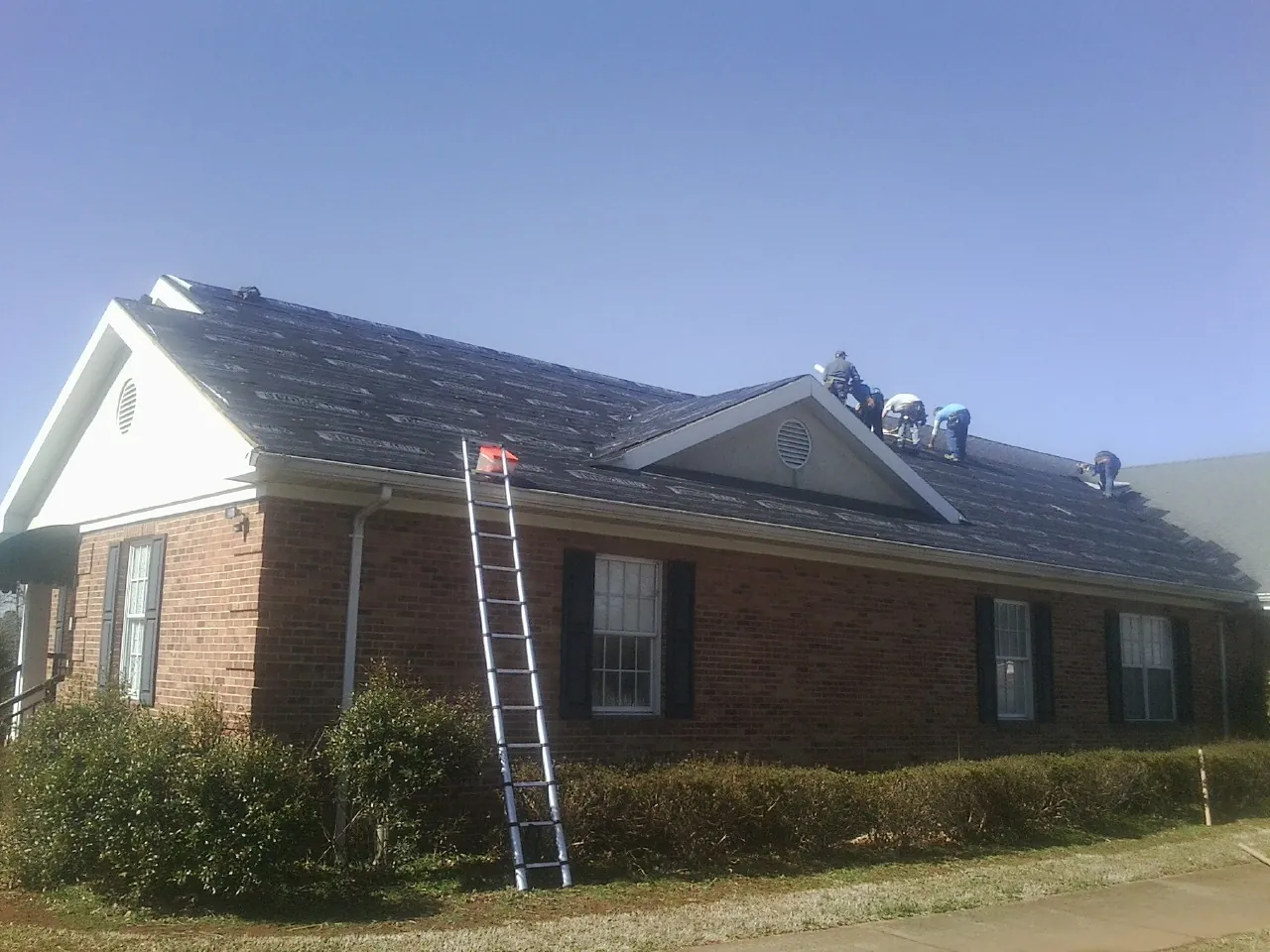 Crew tearing shingles off a brick ranch roof with a ladder set — Emergency Roof Repair work by our crew in Lafayette